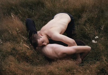 Entrelacés dans les herbes, deux lutteurs, le torse nu. Le visage de l'un, au sol, a disparu derrière le bras de l'autre. Cette photographie de Nolwenn Brod a fait l'objet d'une description en résidence