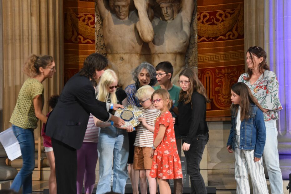 Panthéon. Les enfants reçoivent le trophée du Prix de l'Audace. Marie Diagne Rullier est derrière eux, elle sourit avec bonheur.